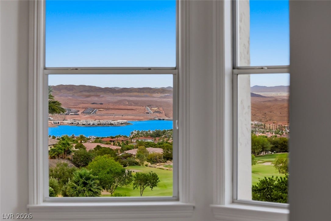 26 Strada Di Circolo, #n/a, Henderson, NV 89011 Large windows frame picturesque desert mountains, a sparkling blue lake, and a lush golf course.