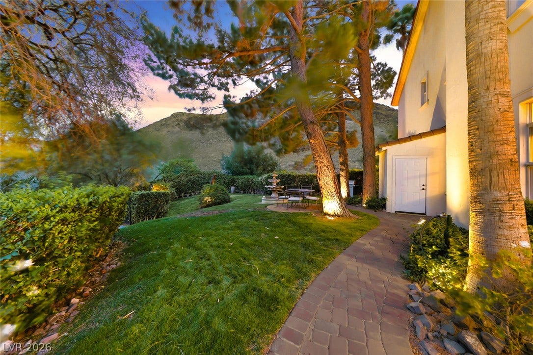 26 Strada Di Circolo, #n/a, Henderson, NV 89011 A paved path winds through manicured lawns beneath mature trees bordering a plaster exterior.