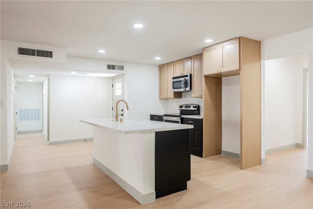 Smooth recessed lighting illuminates this sleek modern kitchen featuring light hardwood-style floors and stone counters.