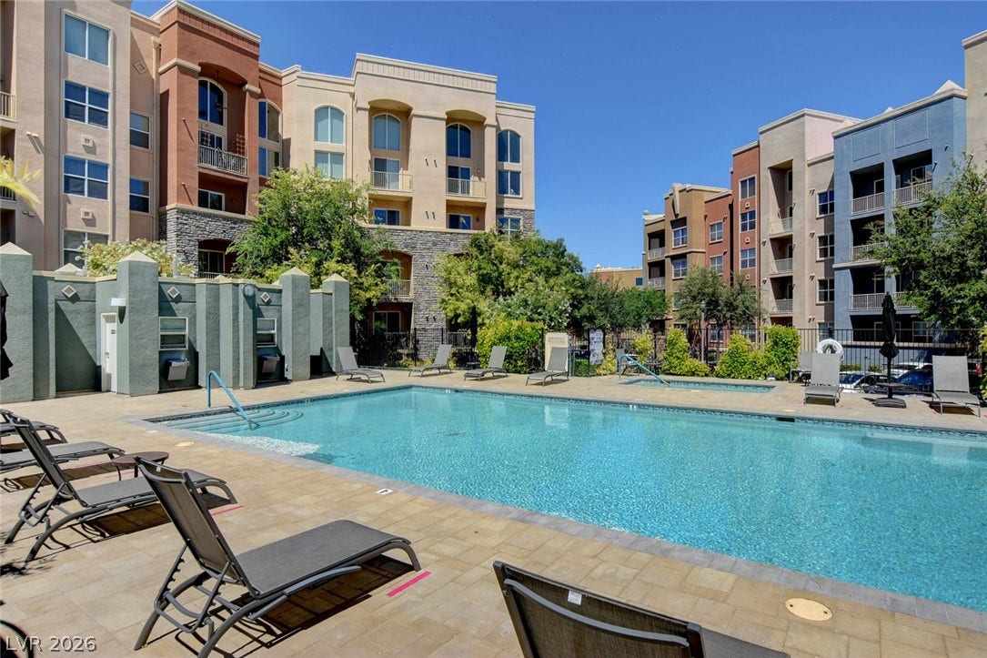 A sparkling swimming pool sits surrounded by stone pavers and multi-level residential structures.