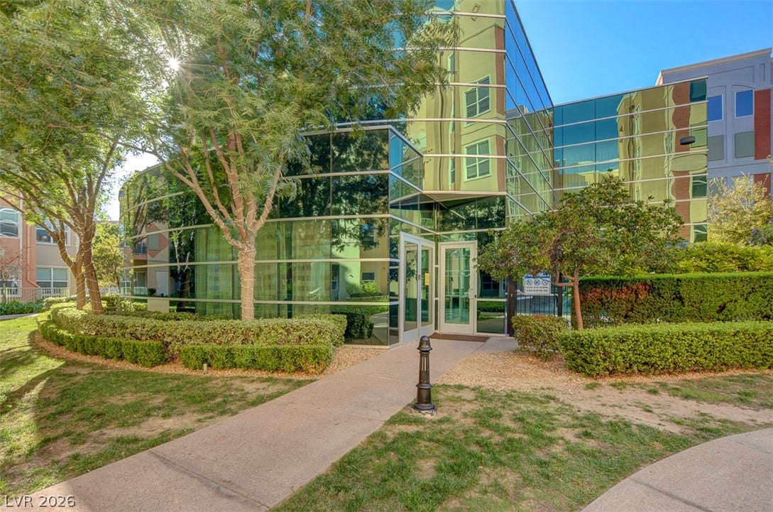 Floor-to-ceiling reflective glass panels wrap the modern exterior alongside a manicured walkway.