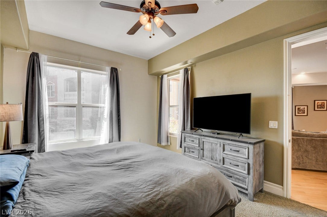 Natural light streams through multiple windows into this comfortable bedroom with soft carpeting.