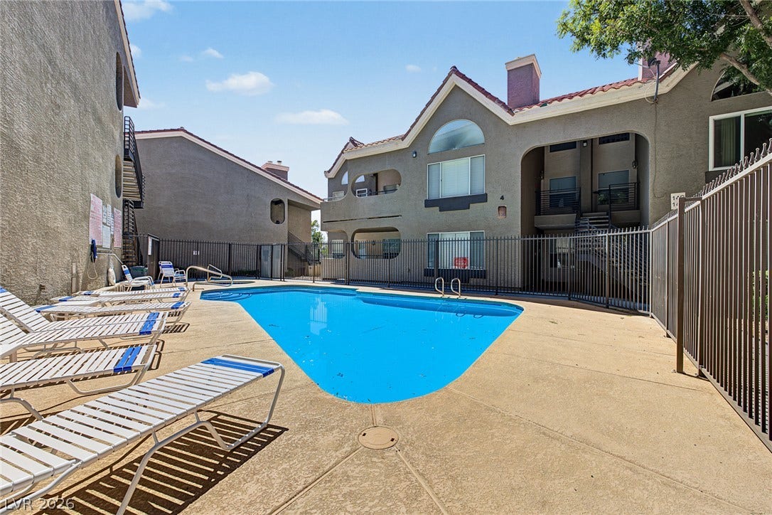701 Capri Drive, #10B, Boulder City, NV 89005 An inviting swimming pool area sits surrounded by classic stucco residential architecture and secure fencing.