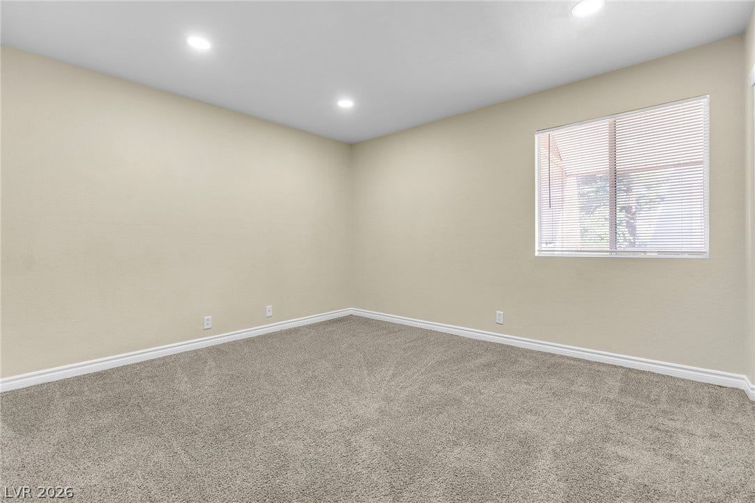 Recessed lighting illuminates this versatile bedroom finished with plush carpeting and crisp white baseboards.