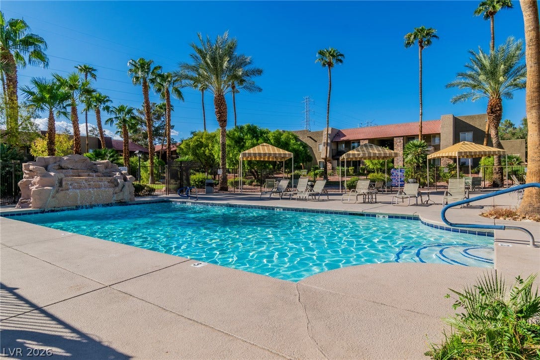 Lush palm trees surround a sparkling blue swimming pool with a stone waterfall feature.