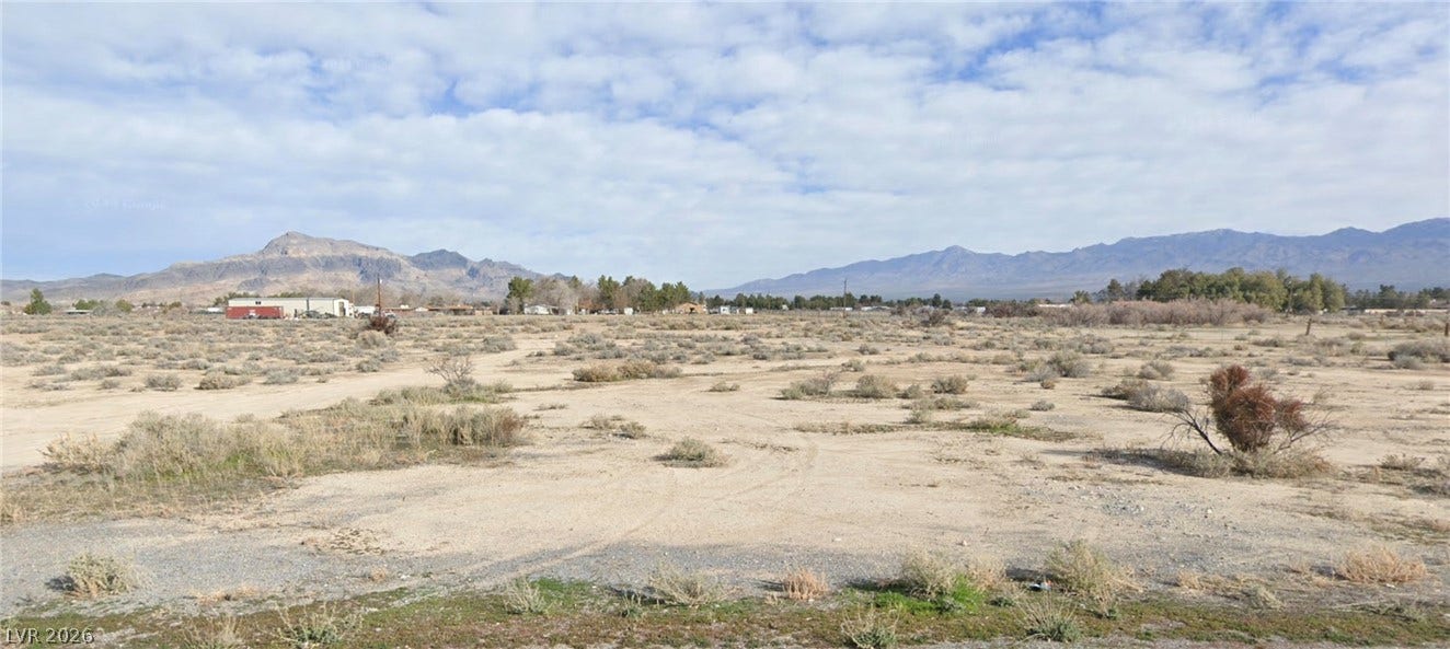 2280 Shady Lane, Pahrump, NV 89060 Rugged desert terrain unfolds toward a majestic mountain backdrop under a partly cloudy sky.