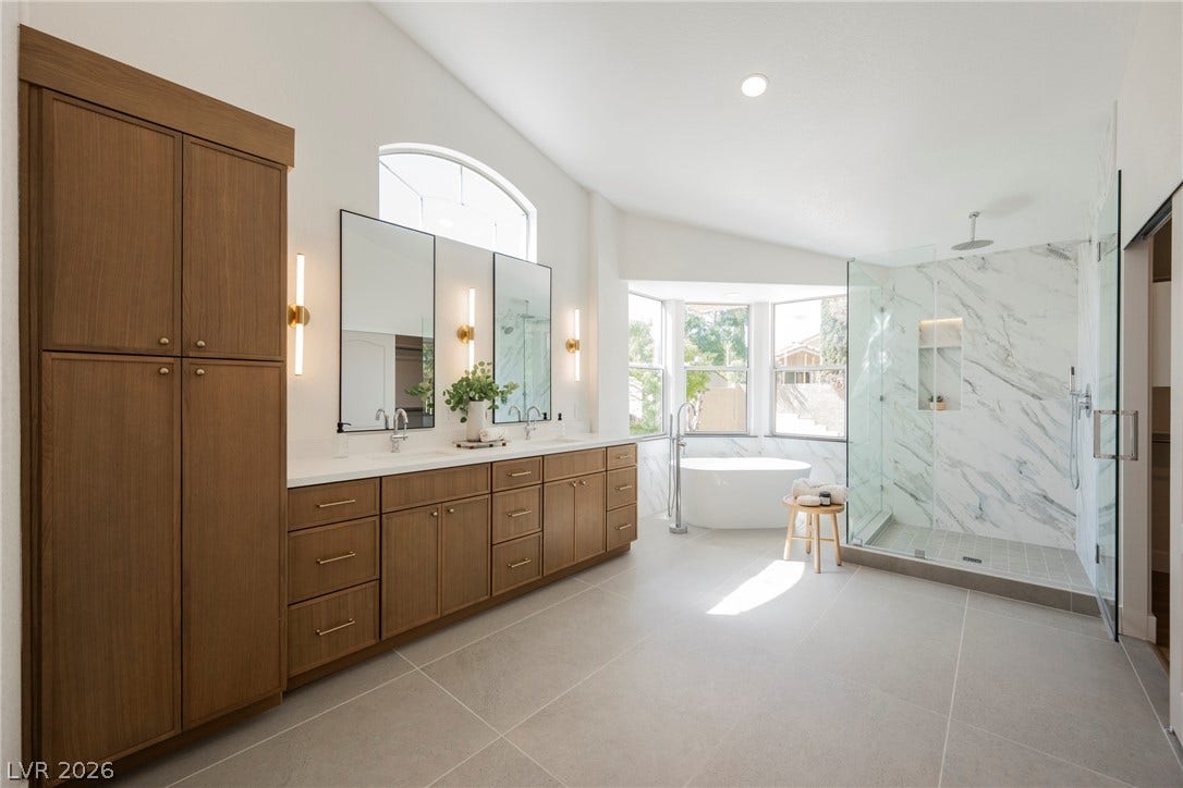 Large tiles run beneath a custom double vanity and a glass-enclosed walk-in shower.