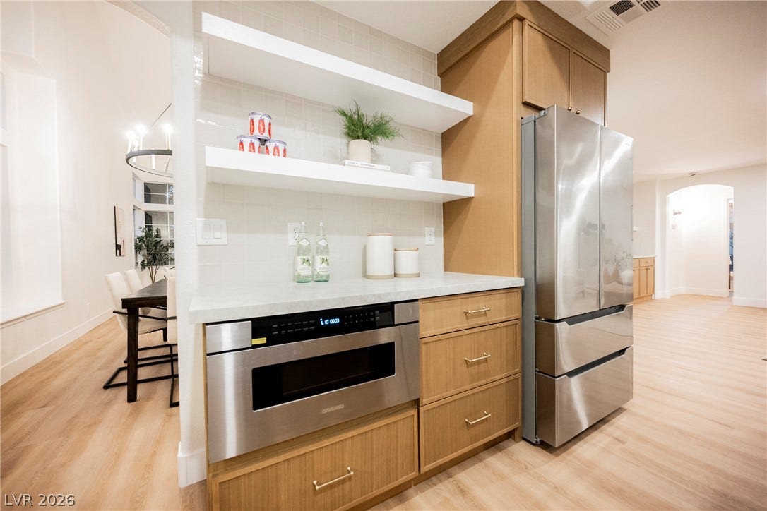 Modern cabinetry and open shelving frame integrated stainless steel appliances over light wood floors.