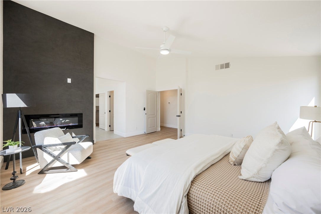 A modern linear fireplace anchors this main bedroom featuring high ceilings and light wood floors.