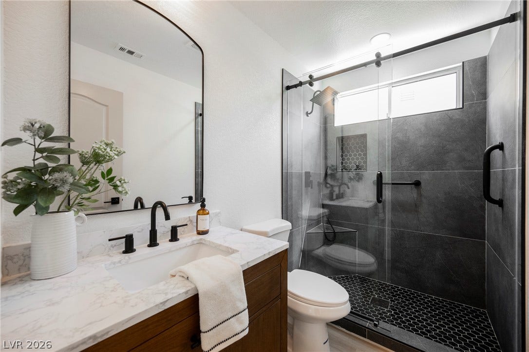 Crisp white walls contrast beautifully with dark walk-in shower tile and rich wood cabinetry.