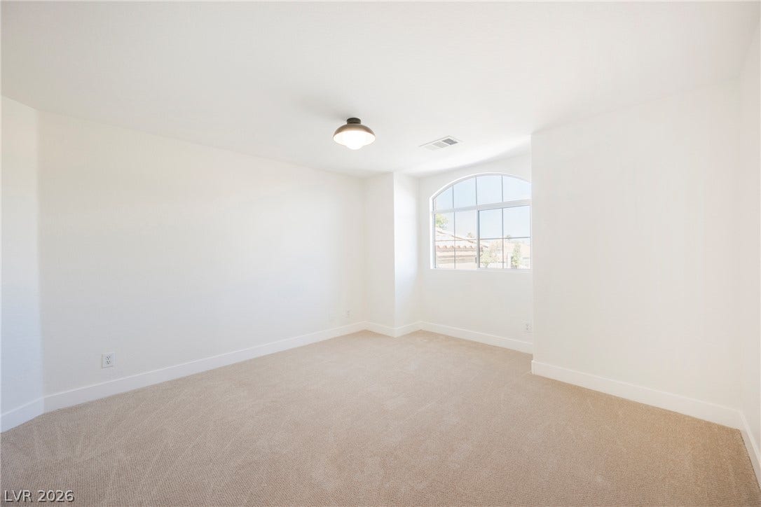 An arched window bathes this carpeted bedroom in rich natural light.