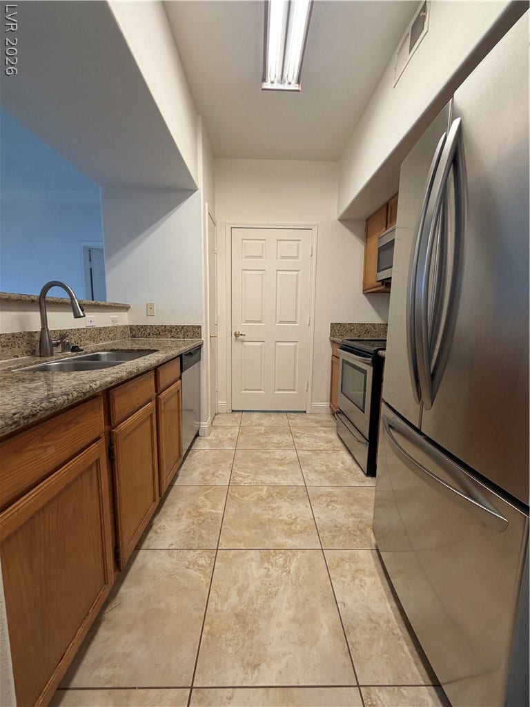 7255 W Sunset Road, #1167, Las Vegas, NV 89113 A galley kitchen features granite countertops, warm wood cabinets, and durable tile flooring.