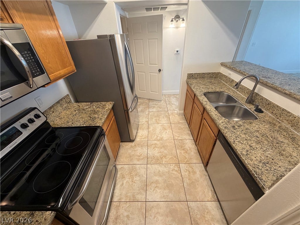 7255 W Sunset Road, #1167, Las Vegas, NV 89113 Granite countertops and rich wood cabinetry anchor this functional galley kitchen layout.