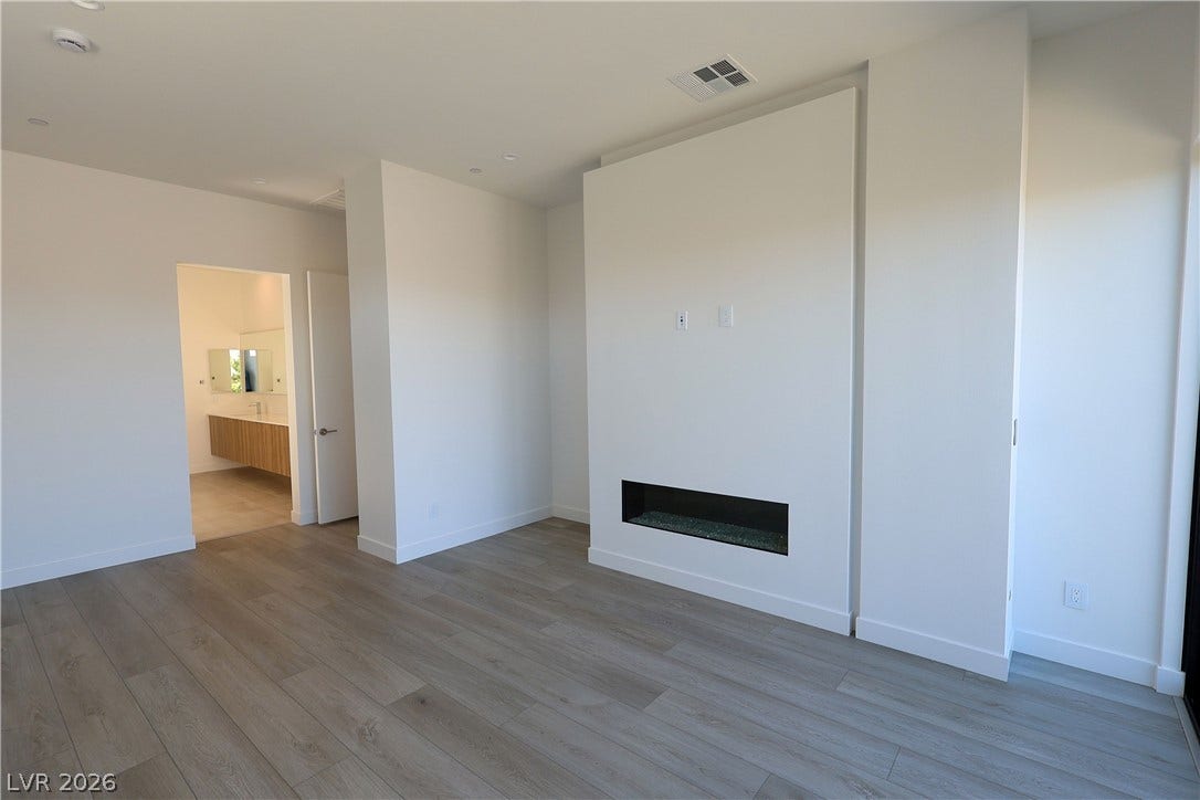 A modern fireplace wall acts as the centerpiece of this spacious bedroom with wood floors.