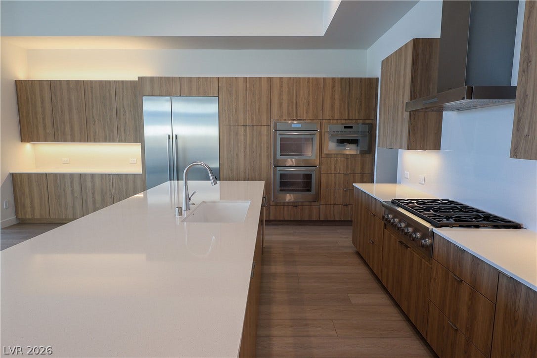 Sleek wooden cabinetry and a massive stone waterfall island anchor this minimalist chef's kitchen.