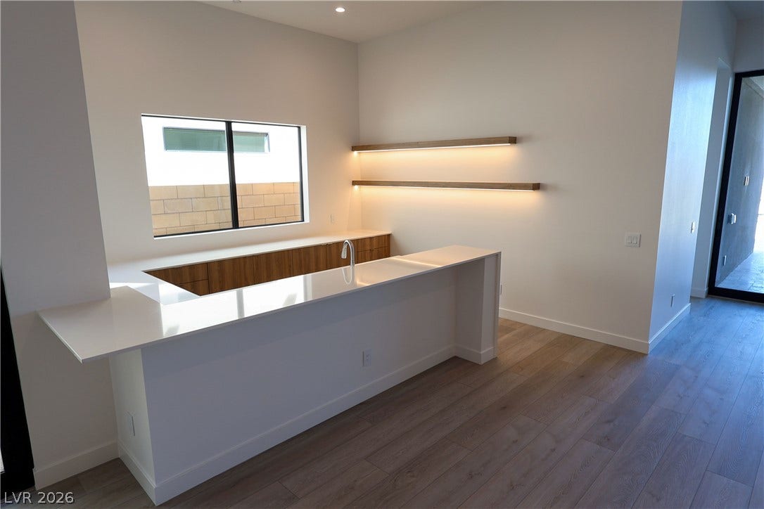 Minimalist design elements highlight this modern wet bar featuring integrated under-shelf lighting and hardwood floors.