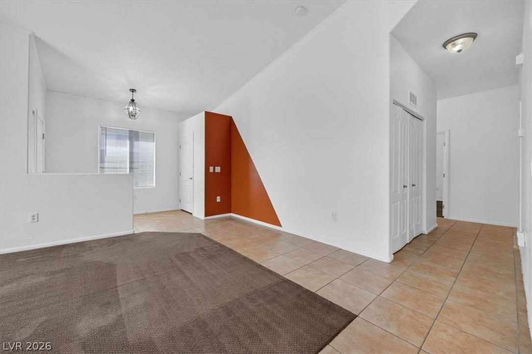 An open layout connects carpeted and tiled living spaces under vaulted ceilings.