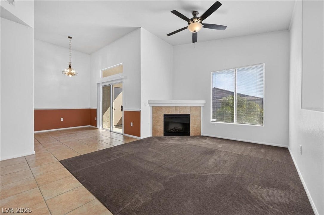 An open floorplan connects the carpeted living area and tiled dining room under high ceilings.