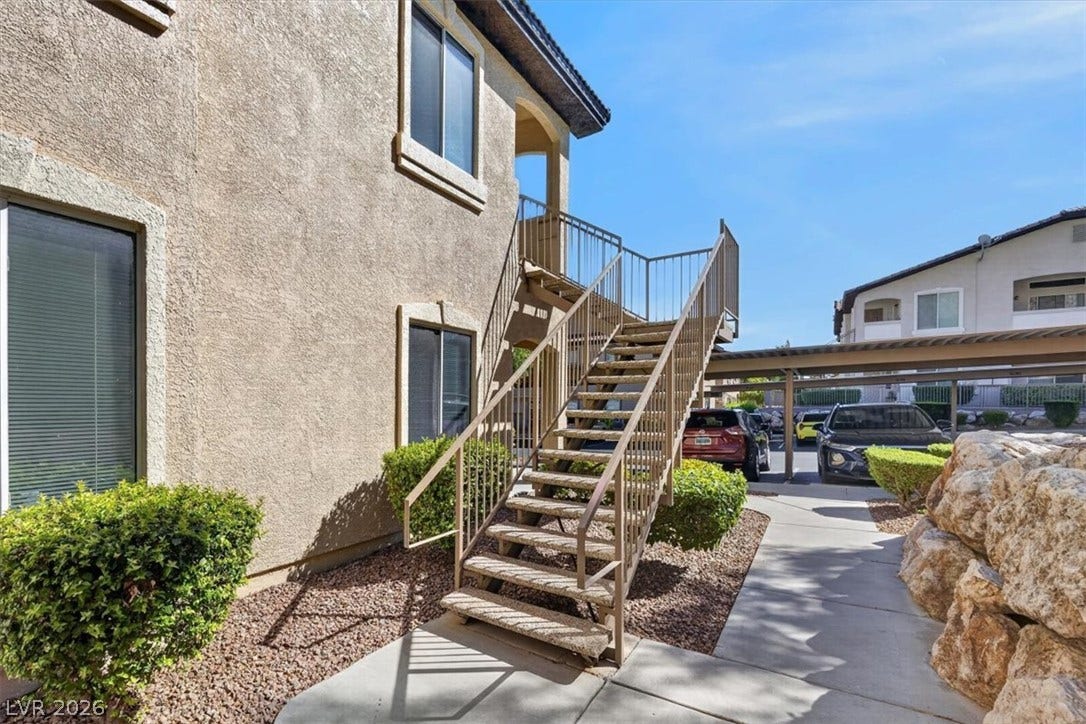Exterior metal stairs ascend past stucco walls along a paved concrete walkway.