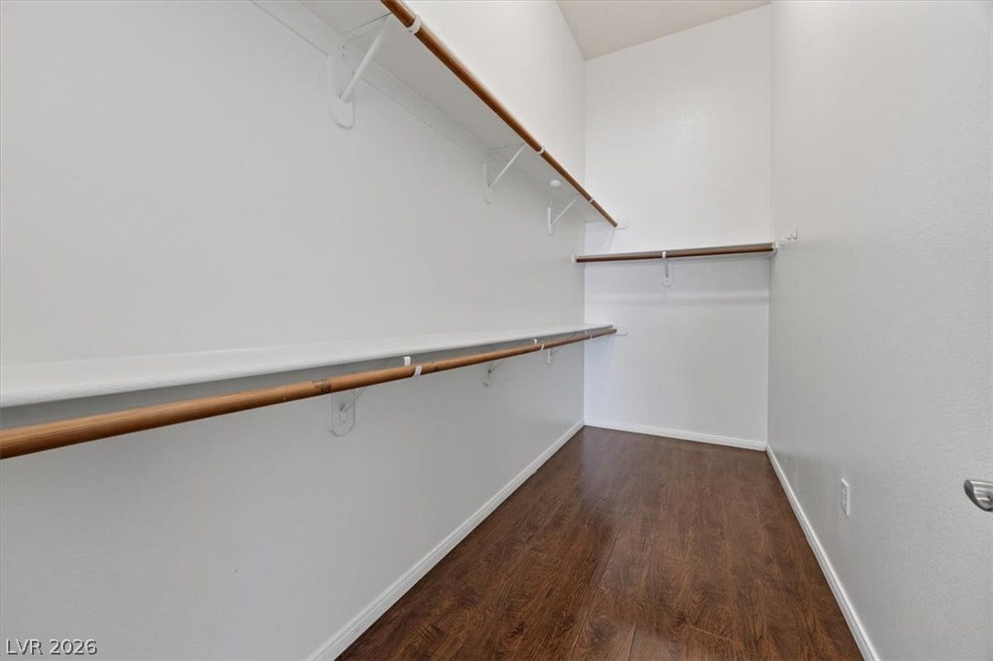 Ample hanging rods and overhead shelving line this closet space featuring rich wood flooring.