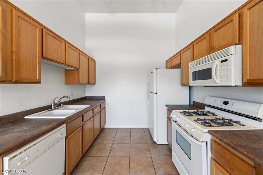 Functional galley kitchen features warm wood cabinetry and neutral tile flooring.