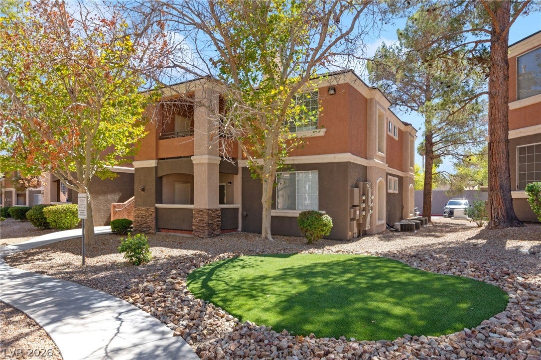 7628 Pacific Hills Avenue, #204, Las Vegas, NV 89128 A paved walkway winds past mature trees toward the stucco exterior of this multi-level residential building.