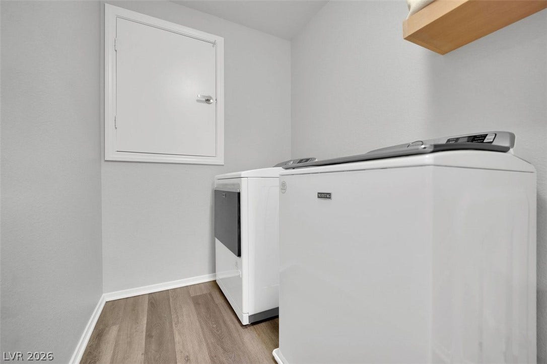 Smooth wood-style flooring anchors this practical laundry space equipped with overhead shelving.