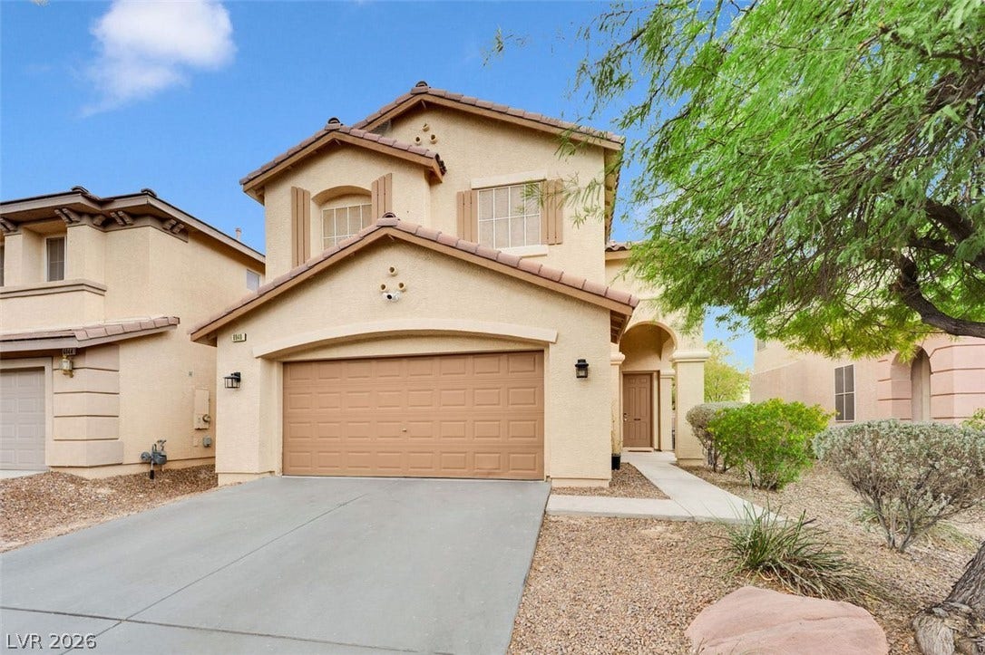 A classic two-story stucco exterior stands behind a concrete driveway and desert landscaping.