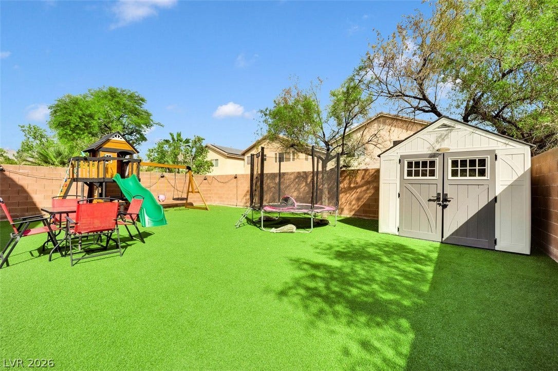 An enclosed backyard features a sprawling synthetic lawn paired with a functional storage shed.