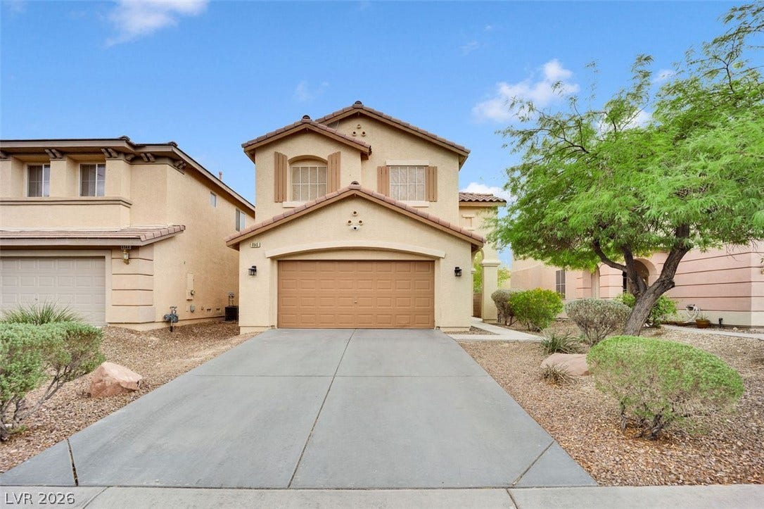 A wide concrete driveway leads toward the integrated garage of this two-story stucco home.