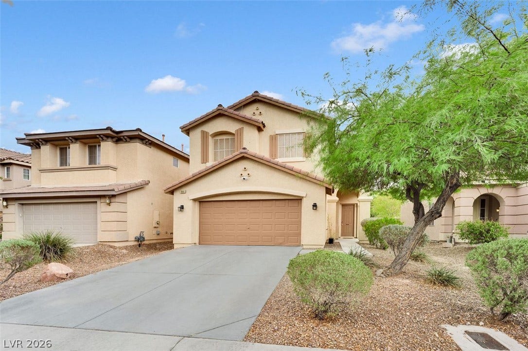 A spacious concrete driveway leads to the attached two-car garage of this multi-level stucco home.