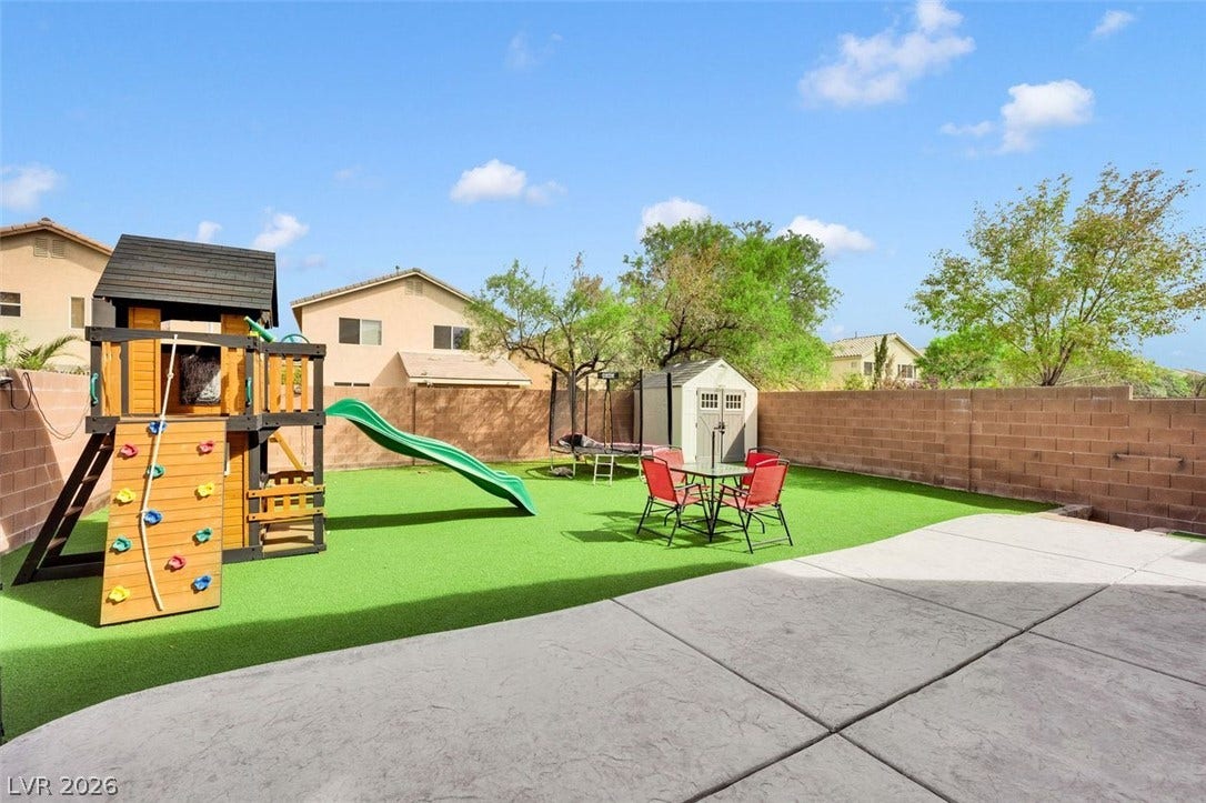 An enclosed backyard features a spacious patio, manicured artificial turf, and a detached storage shed.