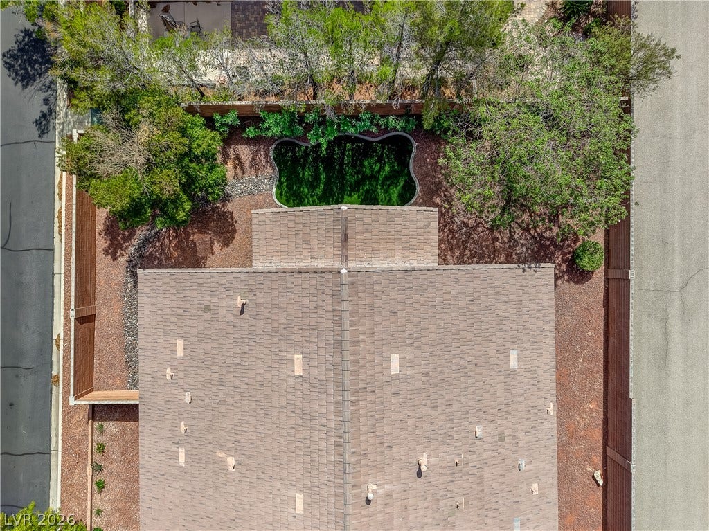 An aerial perspective reveals a shingle roof structure alongside a private yard with mature trees.