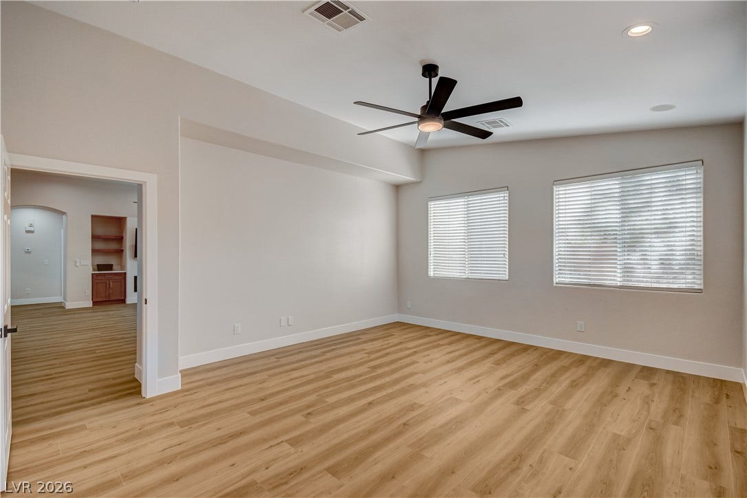 Generous windows fill this versatile bedroom with soft light over smooth wood floors.