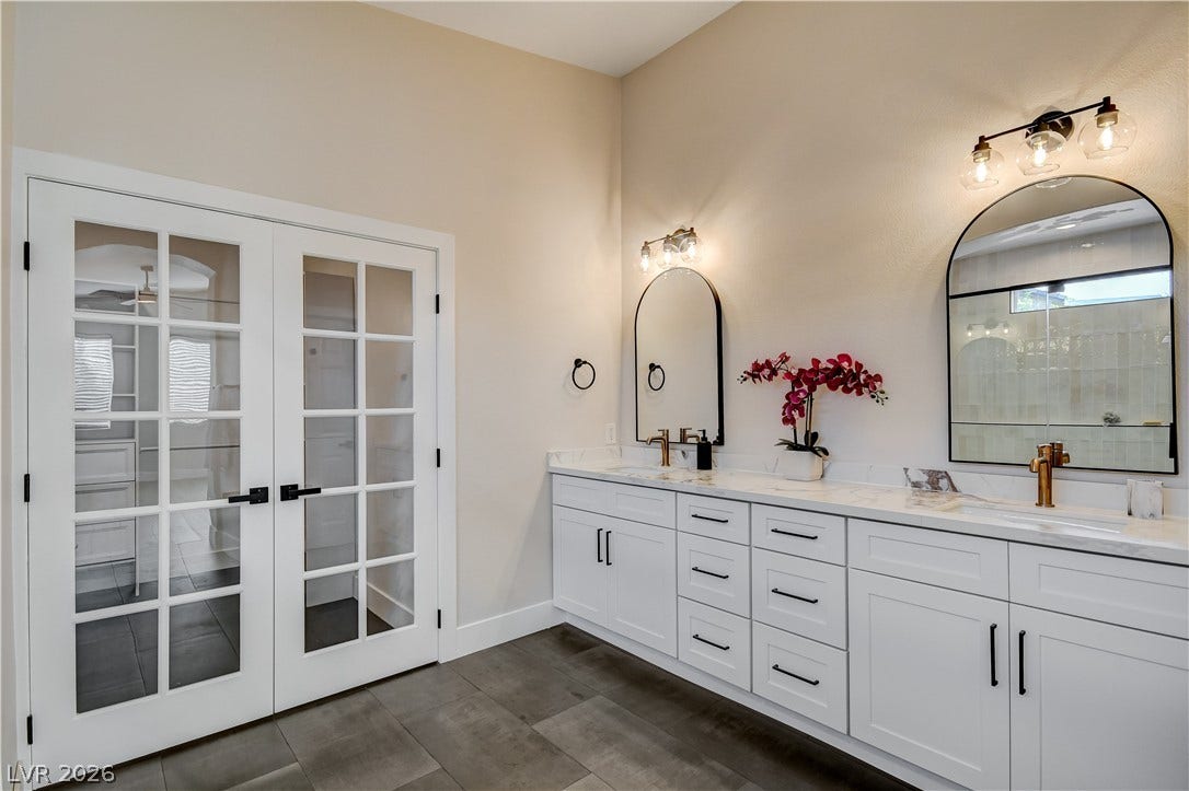 Elegant french doors open into a bright bathroom with a spacious double vanity and modern tiling.