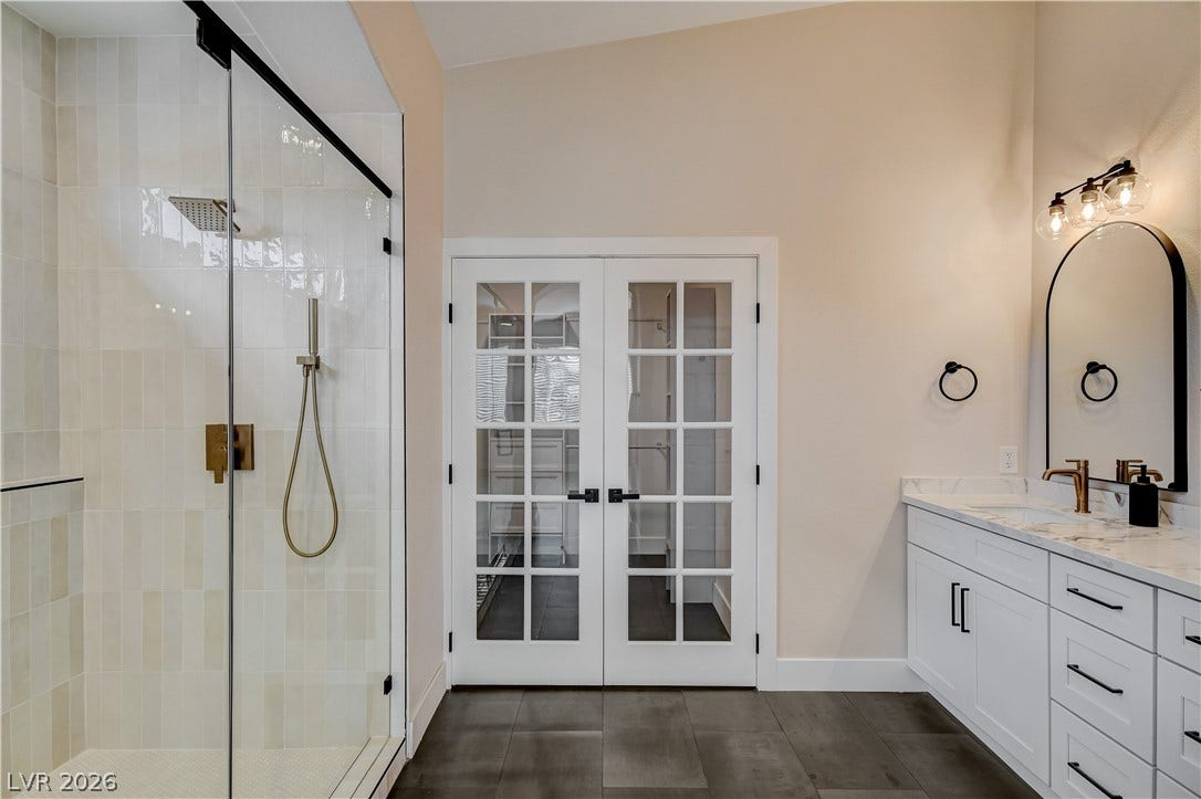 A glass-enclosed shower, stone-look tile flooring, and classic French doors elevate this modern bathroom.
