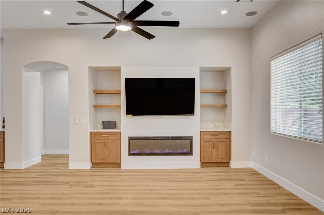 An elegant modern fireplace setup anchors the room alongside built-in shelving and light wood flooring.