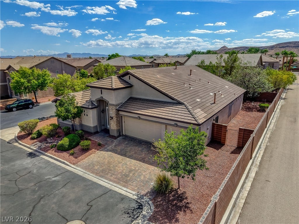 An aerial perspective showcases the stone-accented facade, tile roof, and paver driveway.