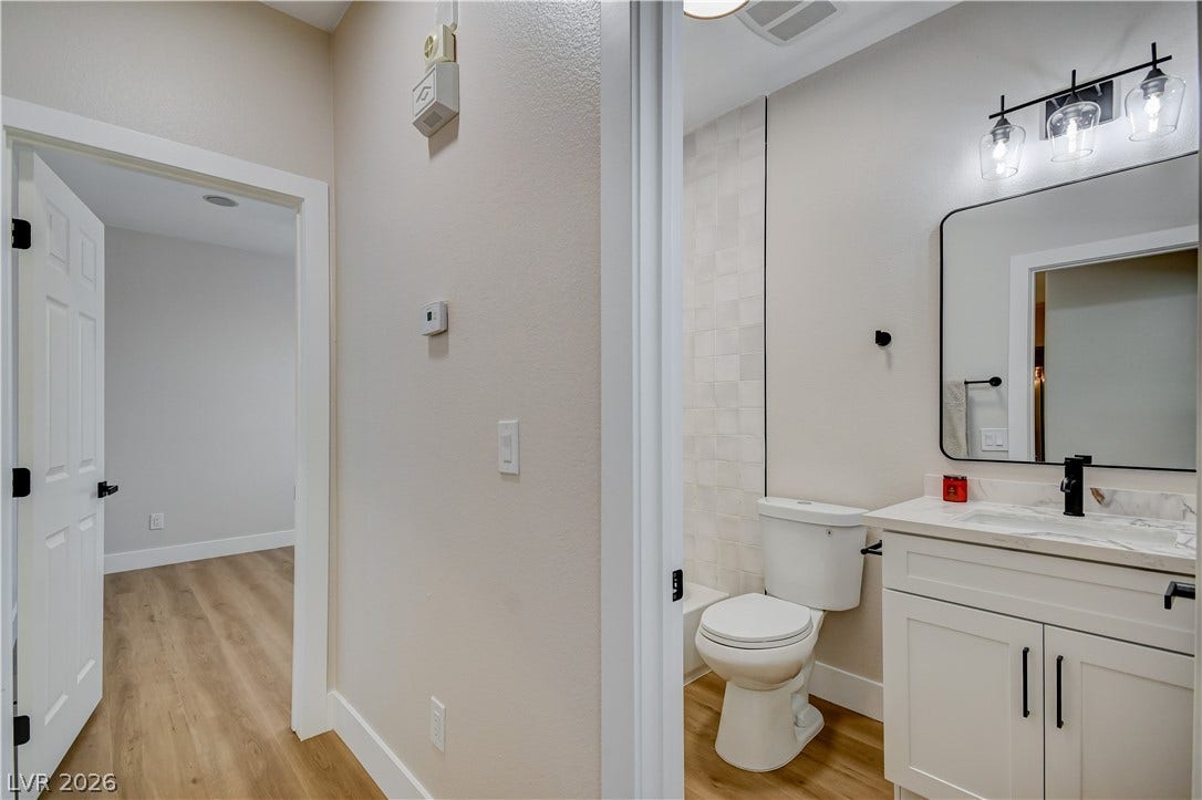A modern vanity with a stone counter sits on wood flooring next to a tiled tub surround.