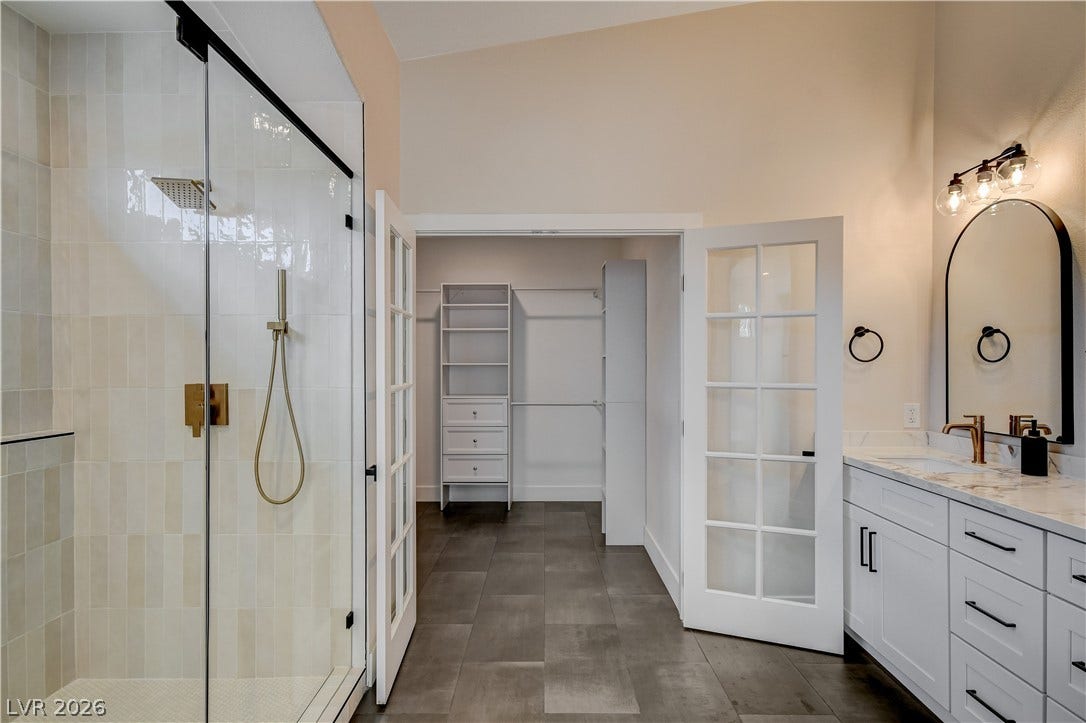 Double glass doors open to a spacious walk-in closet from this modern bathroom.