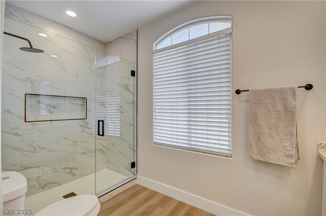 A glass-enclosed shower highlights this modern washroom with warm wood-look flooring.