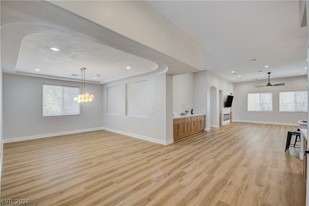 Sweeping wood-look floors anchor a versatile open layout with architectural tray ceilings and modern lighting.