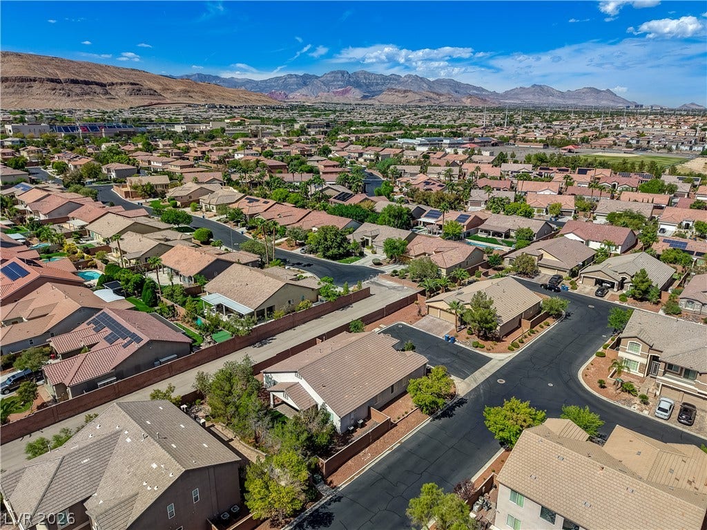 Dramatic mountain ridges frame a peaceful neighborhood of tile-roofed residences under blue skies.