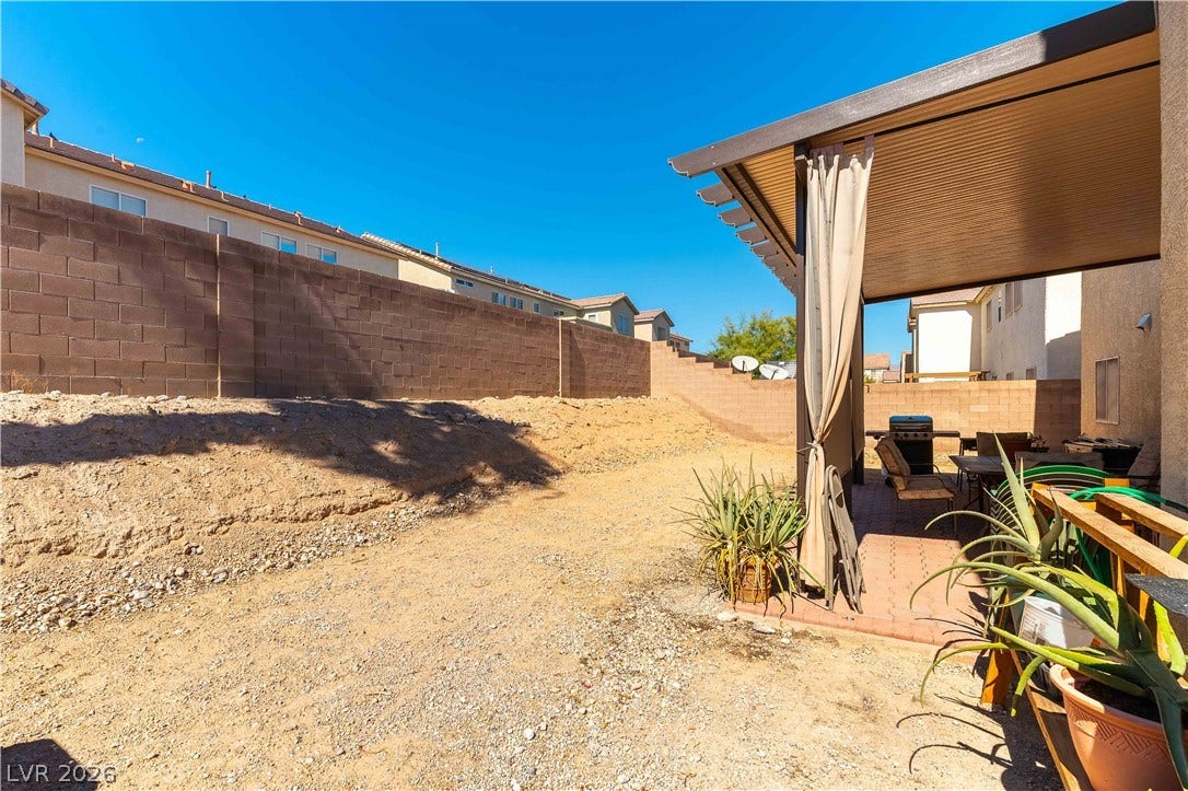 A spacious backyard area includes a covered patio structure alongside a secure block wall.