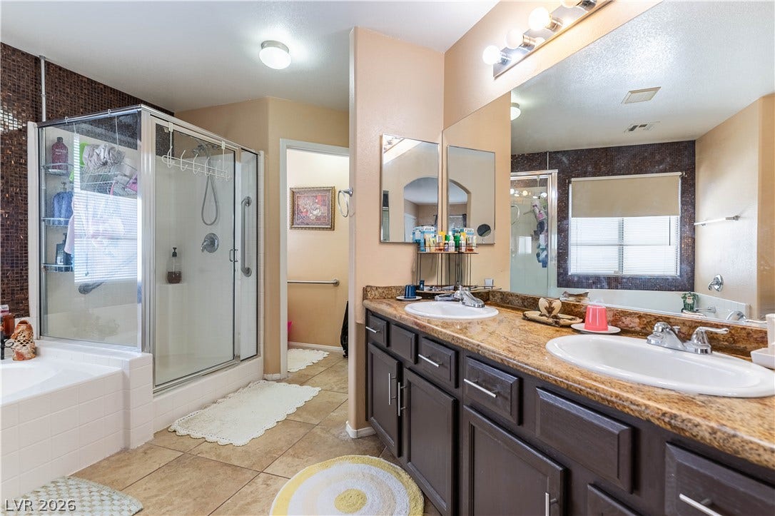 A spacious bathroom features a double vanity with stone countertops and a separate walk-in shower.
