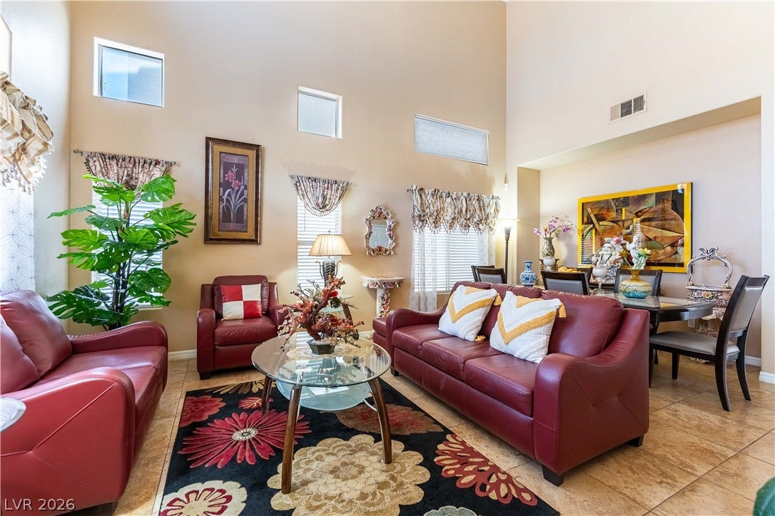 Double-height ceilings and tall windows frame this open-concept living space with tile floors.