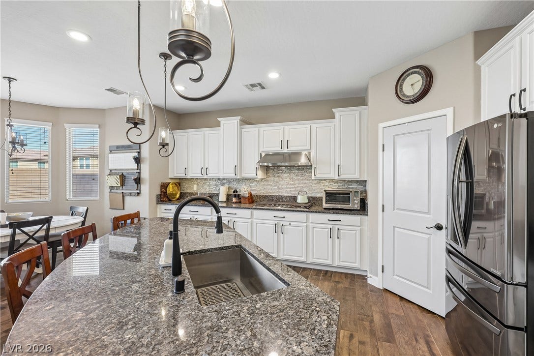 9490 Wild Valley Avenue, Las Vegas, NV 89148 Granite countertops and clean white cabinetry anchor this well-appointed culinary space with warm wood floors.