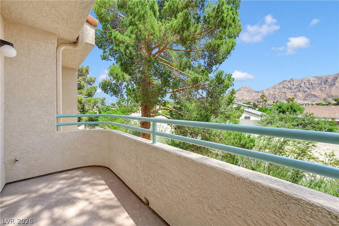 Stucco half-walls with blue railings border a private balcony overlooking mountains.