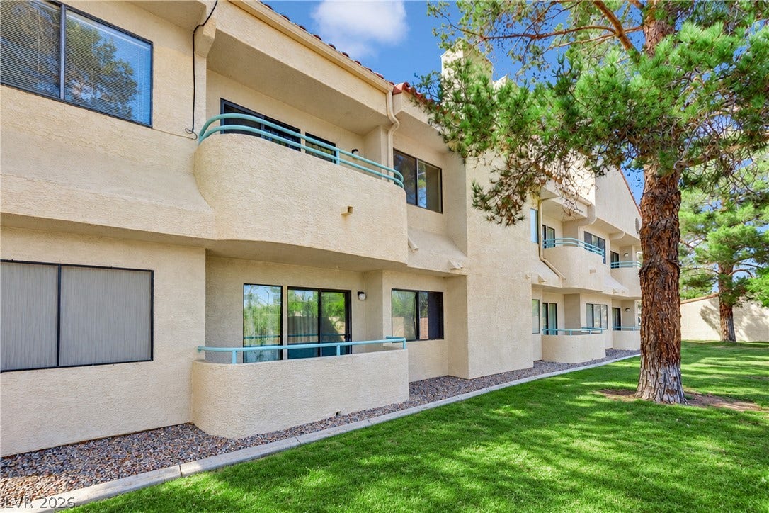 Stucco exteriors and private balconies overlook a manicured lawn bordered by mature trees.