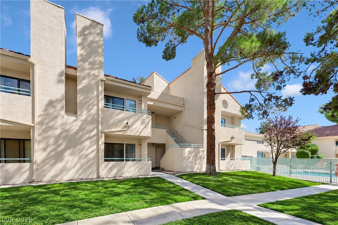 Concrete walkways cross manicured lawns leading toward stucco exteriors under clear skies.